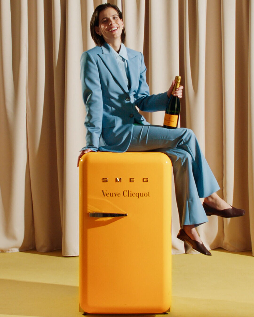 Hand holding Veuve Clicquot champagne above fridge, preparing to chill bubbly