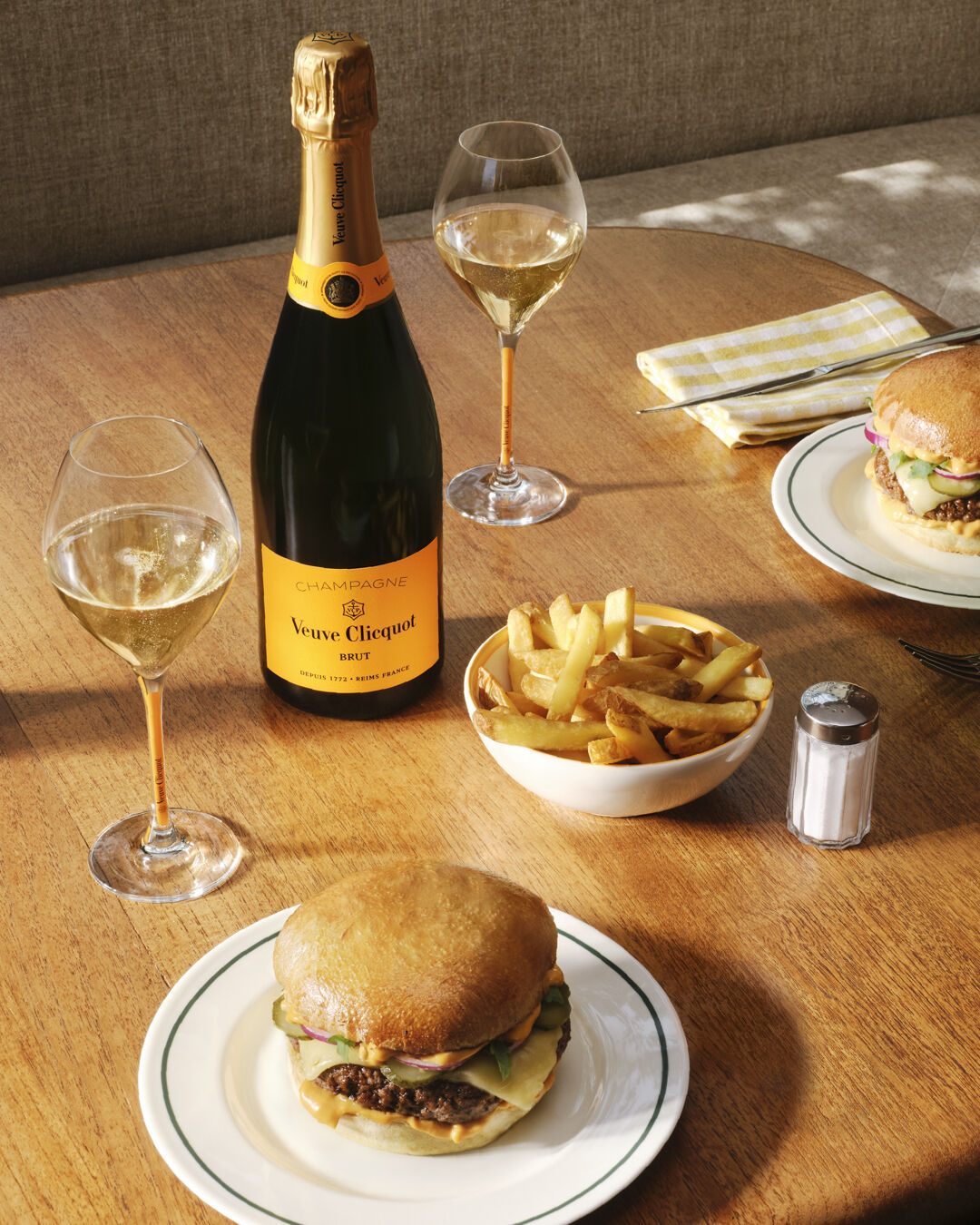 Bouteille de Veuve Clicquot Brut Carte Jaune avec deux verres, un burger et des frites