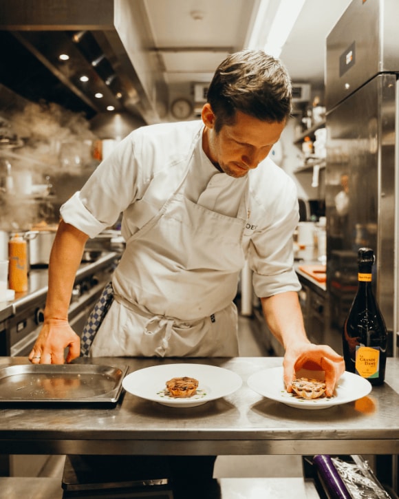 Michaël Vrijmoed serving a plate in the kitchen of his restaurant with a bottle of La Grande Dame 2015