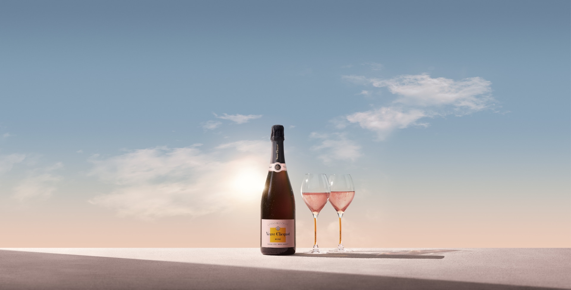 Clicquot Brut Rosé bottle with two full glasses in front of sunrise