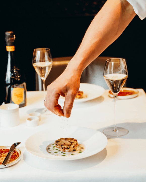 Michaël Vrijmoed serving a plate with two glasses of champagne and a bottle of La Grande Dame 2015
