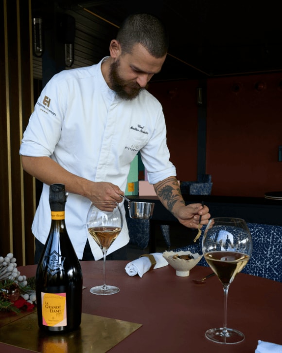 Mattia Trabetti preparing a dish with two glasses of champagne and a bottle of La Grande Dame Rosé 2015