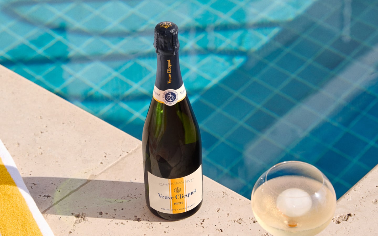 Bottle of RICH champagne with a full glass in front of a swimming pool