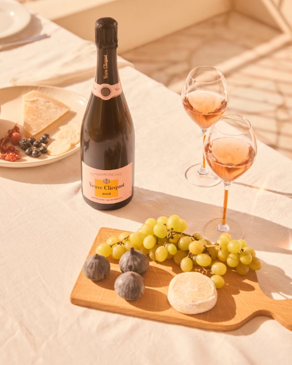 Bottle of Ros&eacute; champagne on a table with two full glasses, fruit and cheese