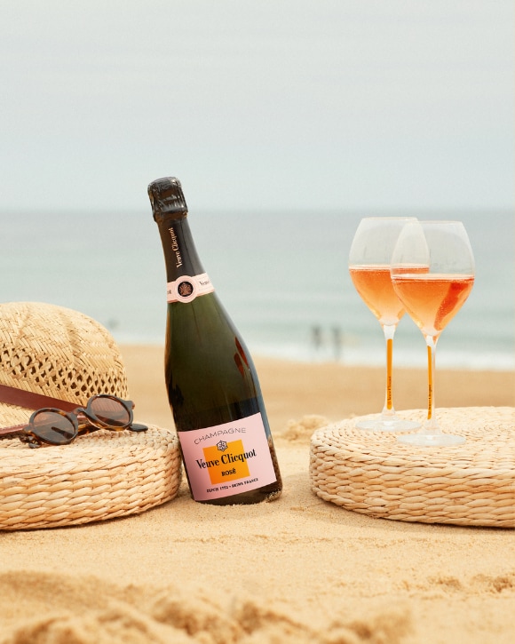 Bottle of Ros&eacute; champagne with two full glasses, in the sand in front of the sea