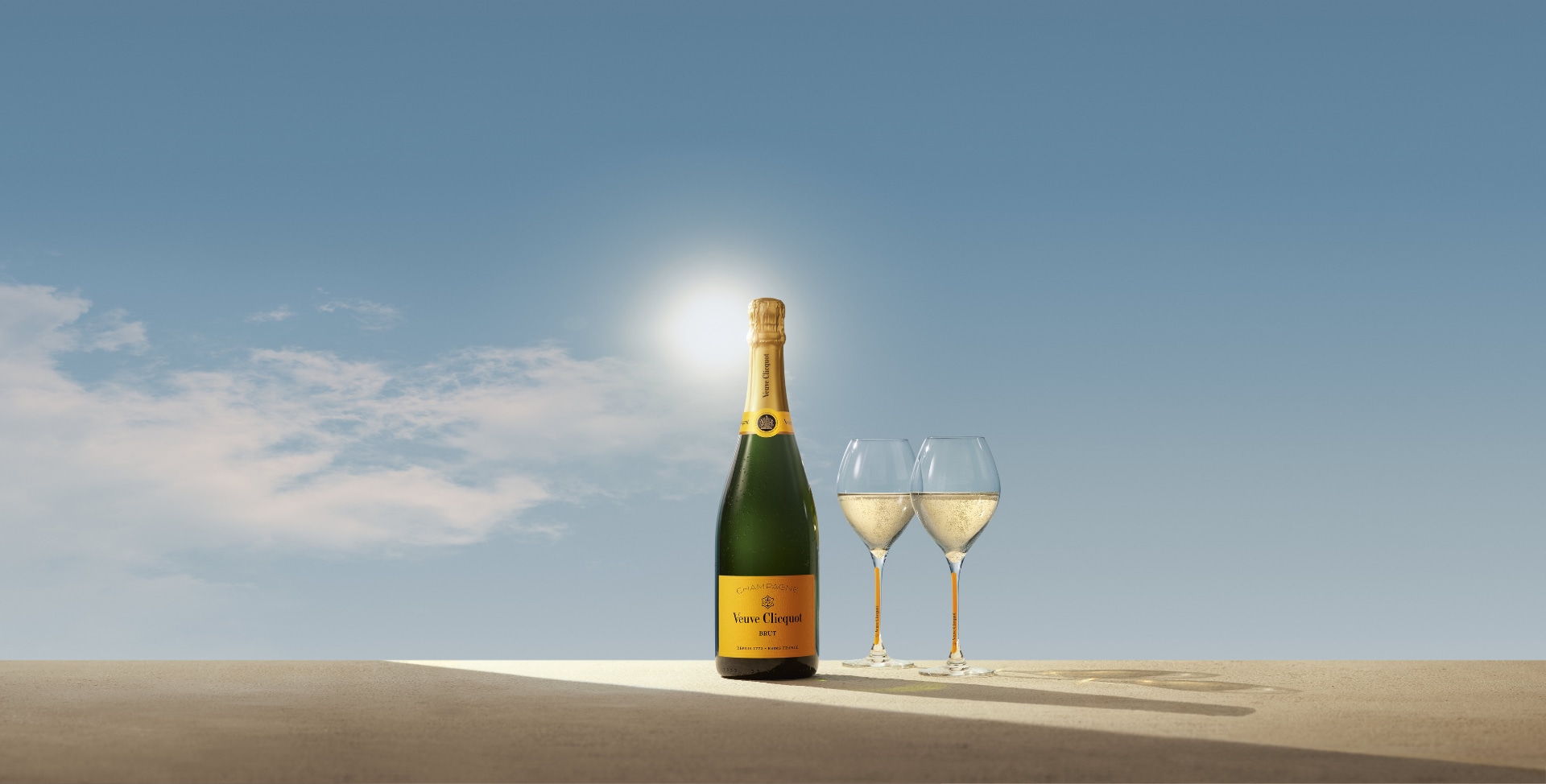 Bottle of Brut Yellow Label champagne with two glasses of champagne in front of a sunrise