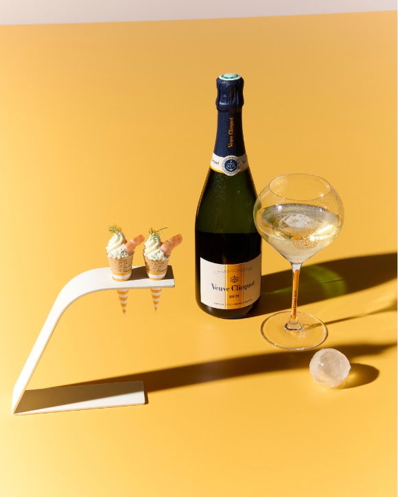Bottle of RICH champagne with a full glass, ice spheres and finger-food